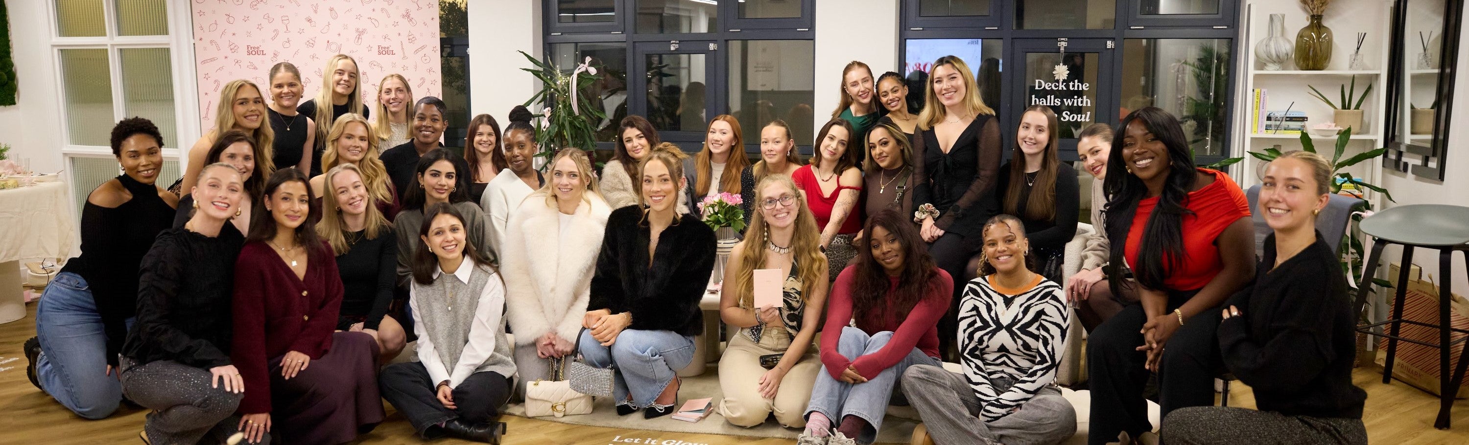A group of people smiling together in a well-lit room with plants.